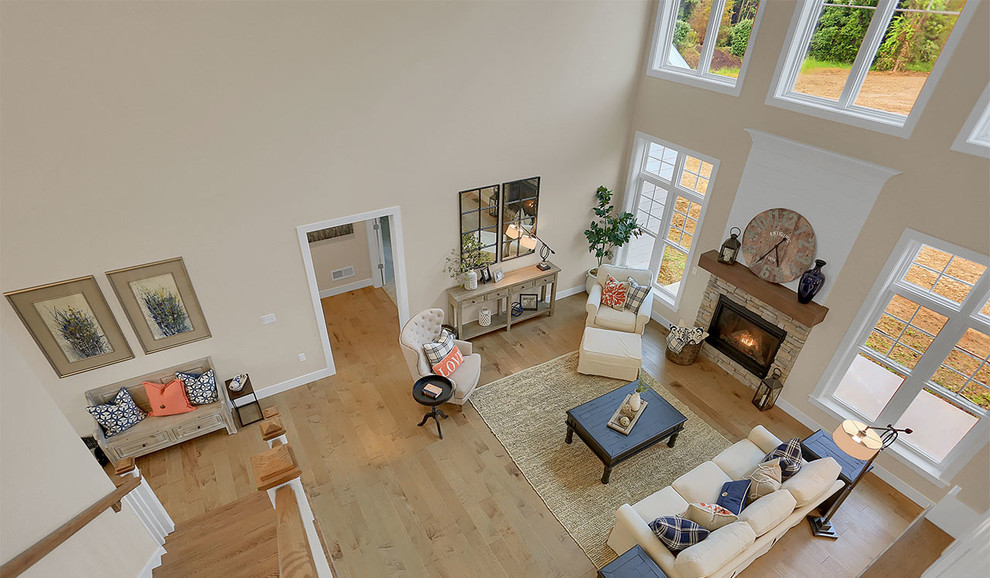 Modelo de sala de estar abierta tradicional extra grande con paredes grises, suelo de madera clara, todas las chimeneas y marco de chimenea de piedra