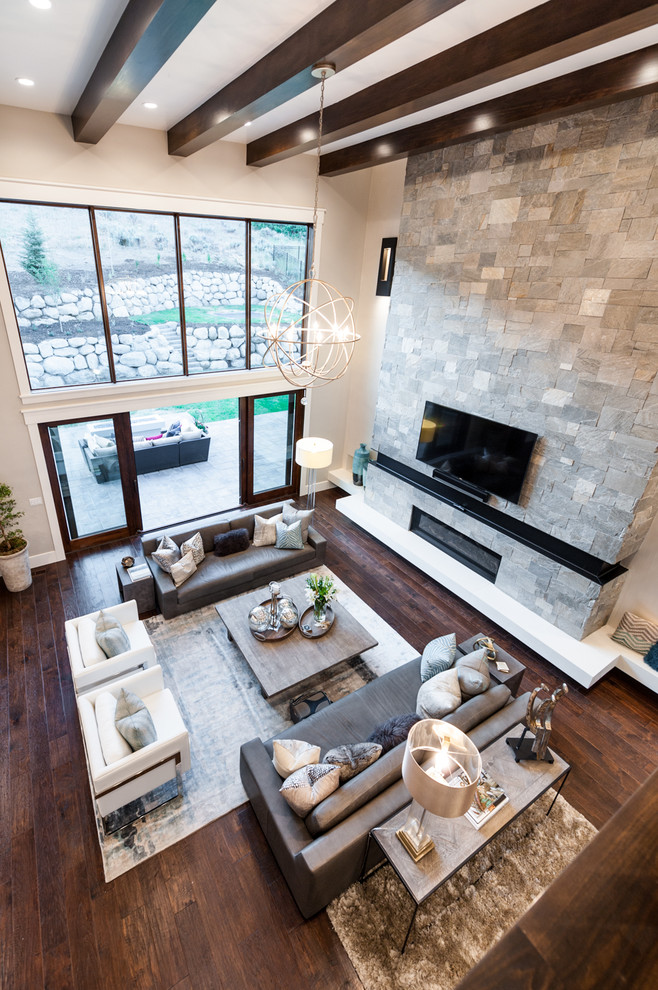 Diseño de sala de estar abierta tradicional renovada de tamaño medio con paredes grises, suelo de madera oscura, todas las chimeneas, marco de chimenea de piedra y televisor colgado en la pared