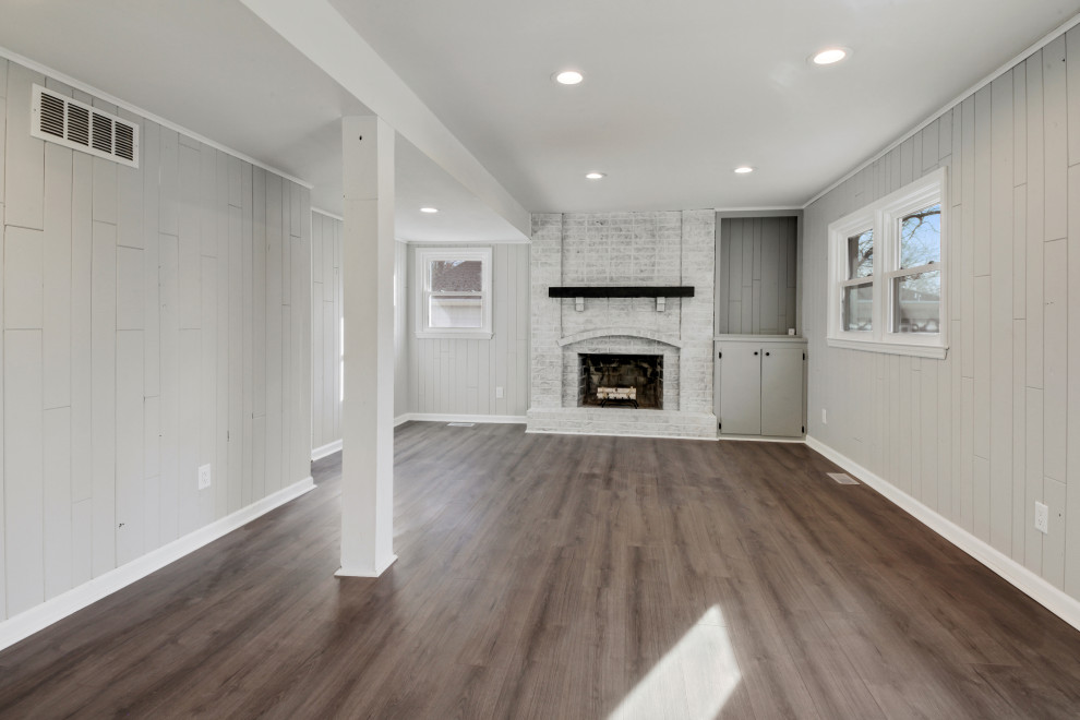 Inspiration for a mid-sized country open concept vinyl floor, gray floor and wall paneling family room remodel in Kansas City with gray walls, a standard fireplace and a brick fireplace
