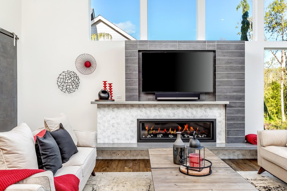 Cette image montre une grande salle de séjour urbaine ouverte avec un mur blanc, un sol en bois brun, un manteau de cheminée en carrelage, un téléviseur fixé au mur et un sol marron.