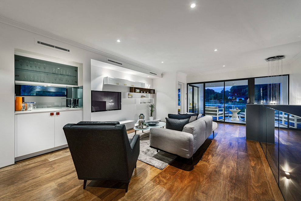 Modelo de sala de estar contemporánea sin chimenea con paredes blancas, suelo de madera en tonos medios y televisor colgado en la pared