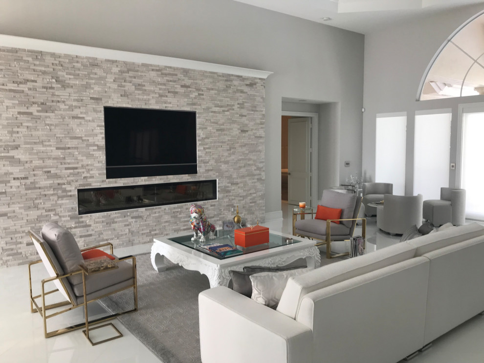 Modelo de sala de estar abierta minimalista grande con suelo blanco, paredes beige, suelo de baldosas de porcelana, chimenea lineal, marco de chimenea de piedra y pared multimedia