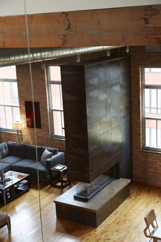 Imagen de sala de estar tipo loft industrial de tamaño medio sin televisor con suelo de madera clara, chimenea de doble cara, marco de chimenea de metal y suelo marrón