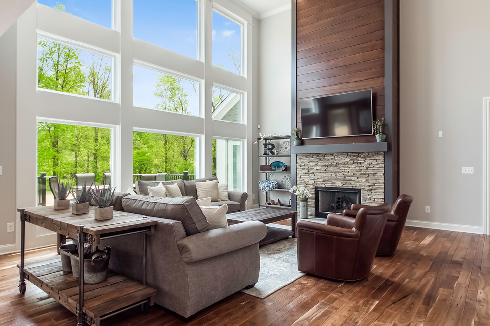 This is an example of a classic open plan games room in Columbus with grey walls, medium hardwood flooring, a standard fireplace, a stone fireplace surround, a wall mounted tv and brown floors.