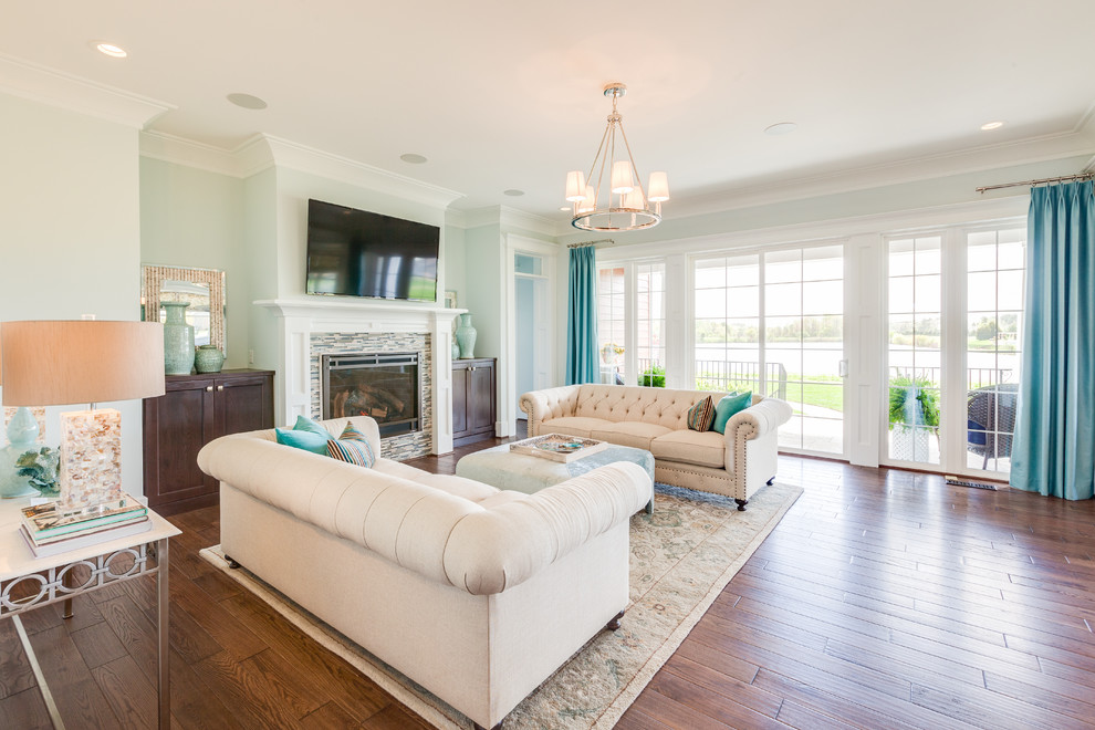 Imagen de sala de estar abierta de estilo americano con paredes azules, suelo de madera en tonos medios, todas las chimeneas, marco de chimenea de baldosas y/o azulejos y televisor colgado en la pared