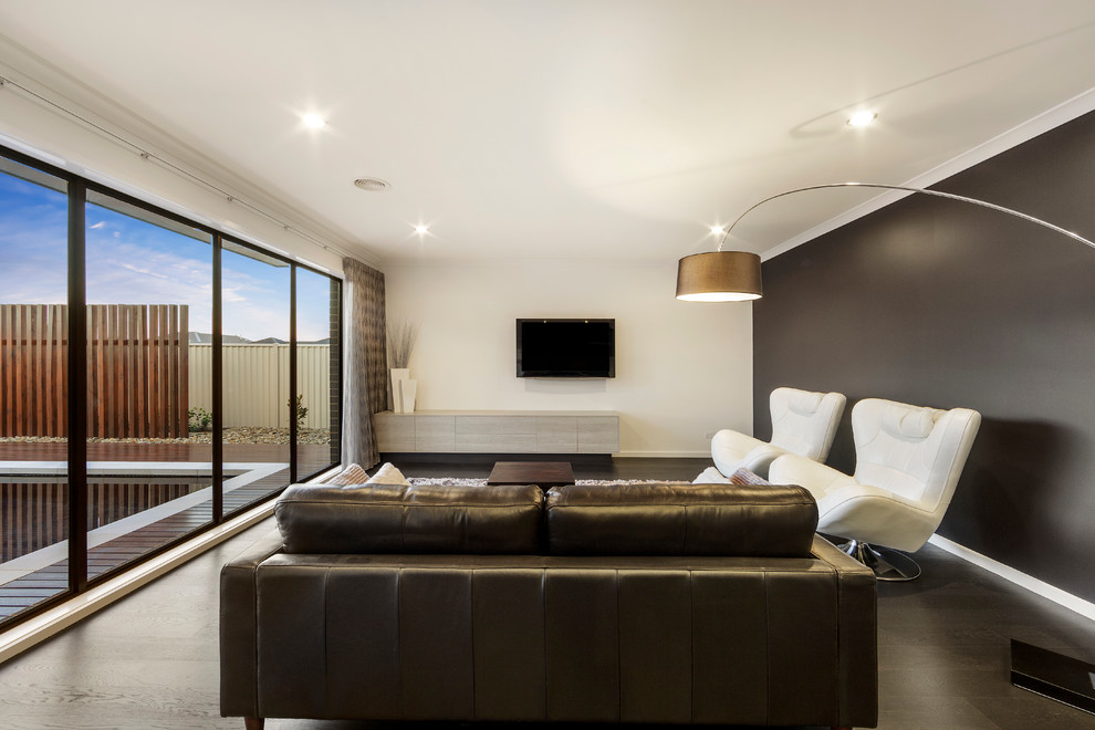 Imagen de sala de estar abierta minimalista de tamaño medio con paredes grises, suelo de madera oscura y televisor colgado en la pared