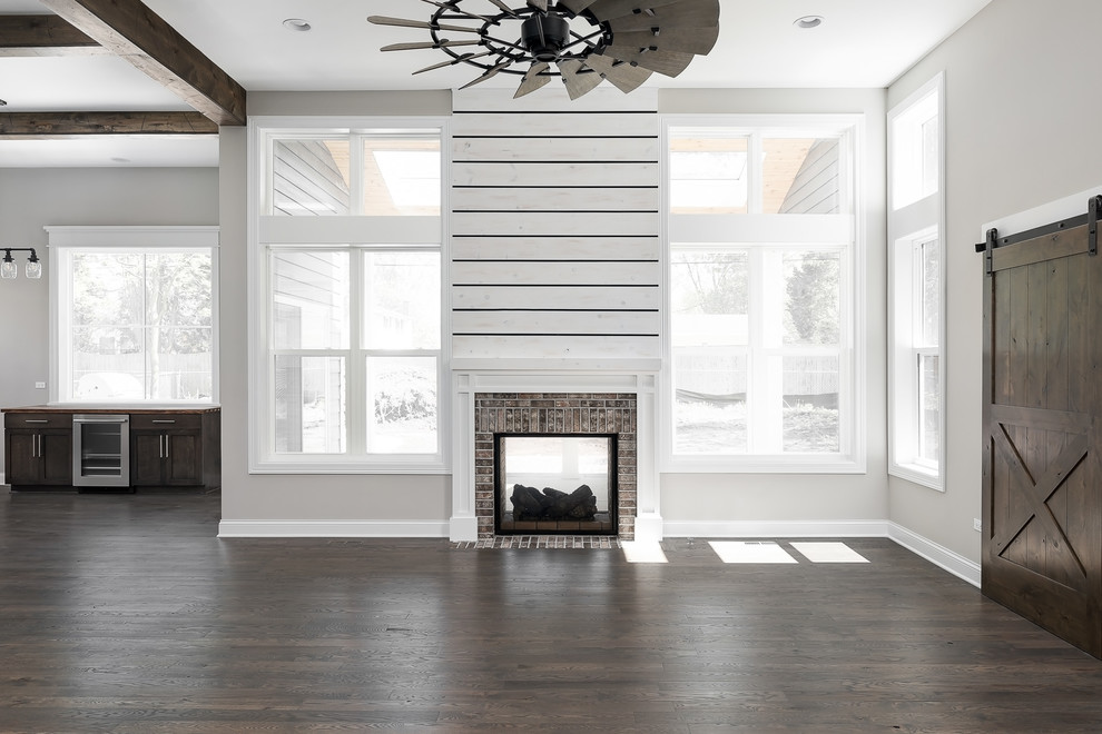 Inspiration for a large country open plan games room in Chicago with beige walls, dark hardwood flooring, a two-sided fireplace, a wooden fireplace surround and brown floors.