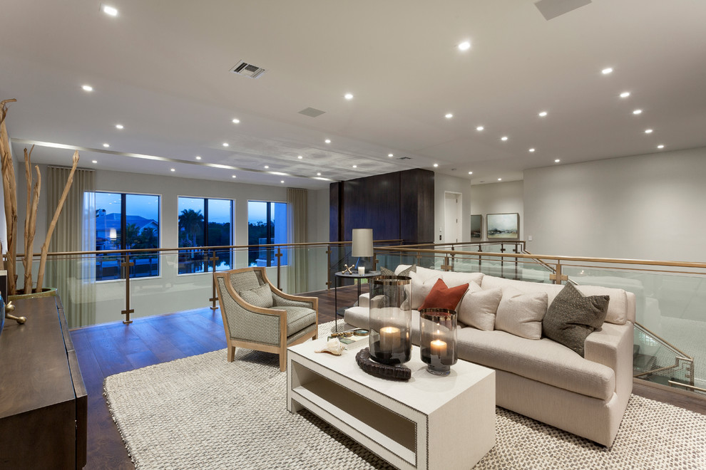 Diseño de sala de estar abierta actual extra grande con paredes grises, suelo de madera en tonos medios y televisor colgado en la pared
