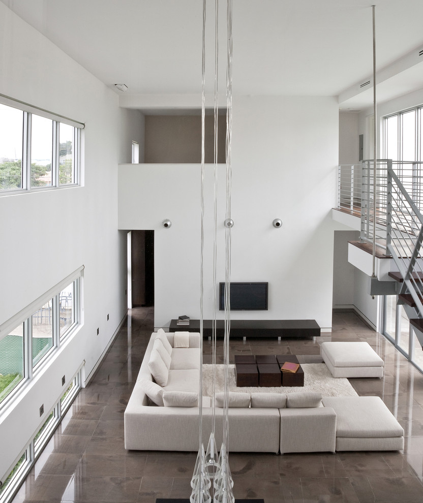 Réalisation d'une grande salle de séjour minimaliste ouverte avec un mur blanc, sol en béton ciré et un téléviseur fixé au mur.