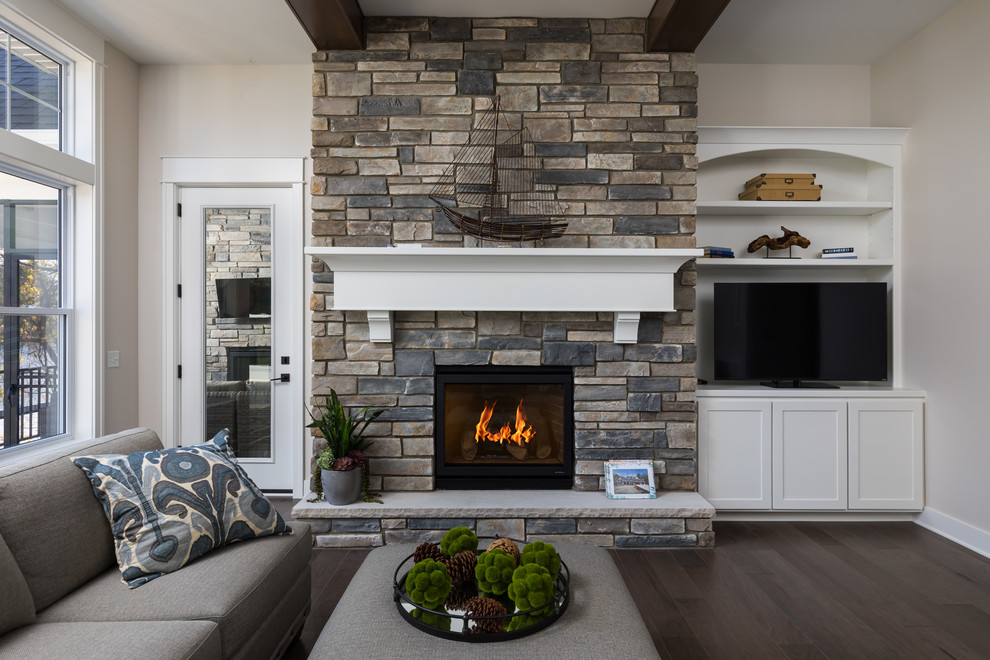 Imagen de sala de estar costera con todas las chimeneas, marco de chimenea de piedra, suelo marrón, paredes beige, suelo de madera oscura y pared multimedia