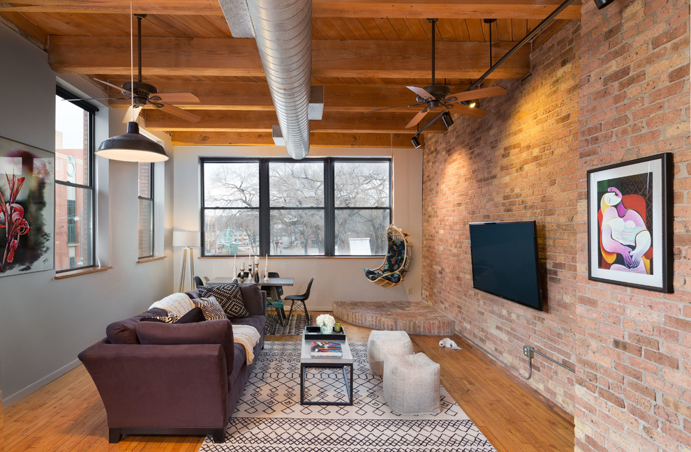 Modelo de sala de estar abierta urbana grande sin chimenea con suelo de madera en tonos medios, televisor colgado en la pared y paredes grises