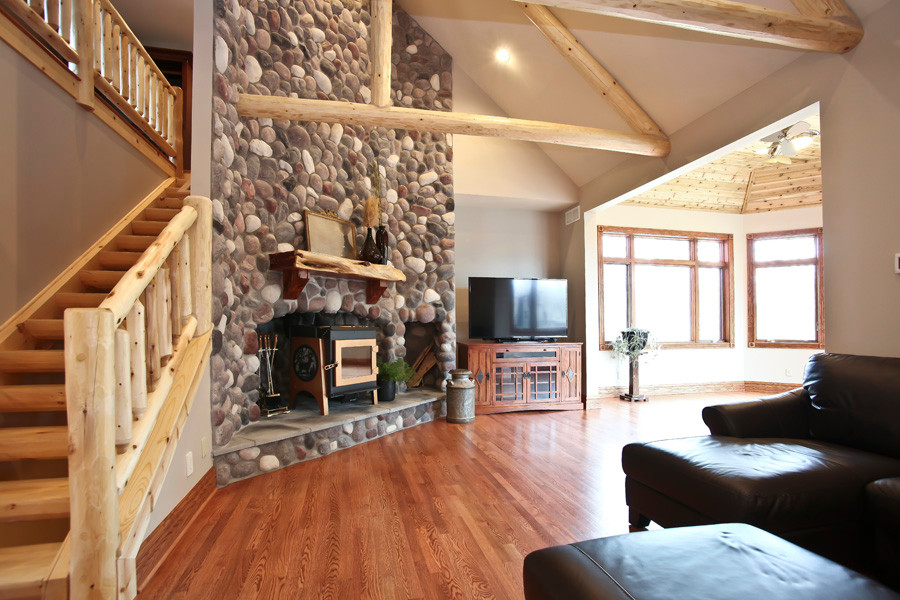 Ejemplo de sala de estar abierta rural grande con paredes beige, suelo de madera en tonos medios, chimenea de esquina, marco de chimenea de piedra y televisor independiente