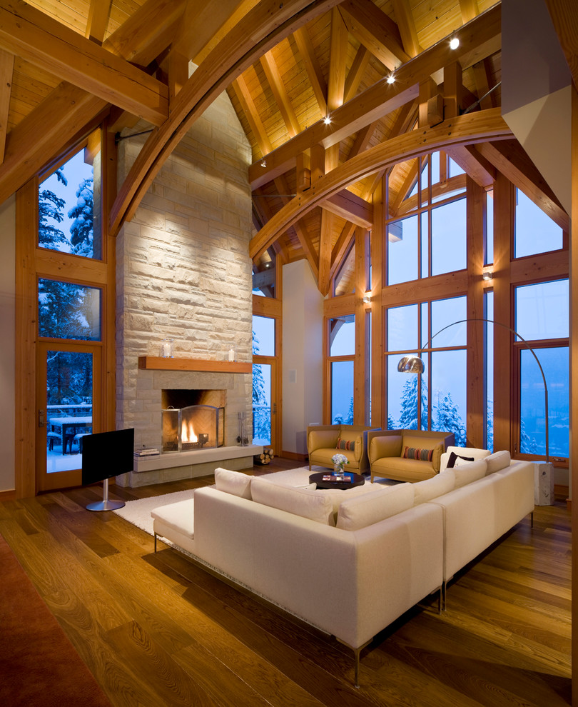 Diseño de sala de estar abierta rústica grande con suelo de madera en tonos medios, todas las chimeneas, marco de chimenea de piedra, televisor independiente y paredes beige