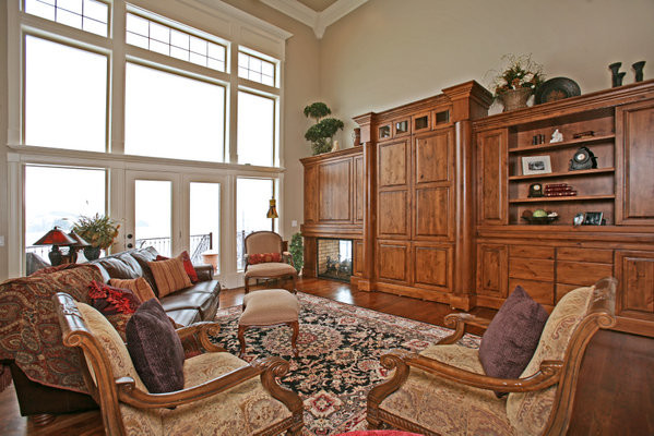 Modelo de sala de estar abierta tradicional grande con paredes beige, suelo de madera en tonos medios, chimenea de doble cara, marco de chimenea de madera y televisor retractable
