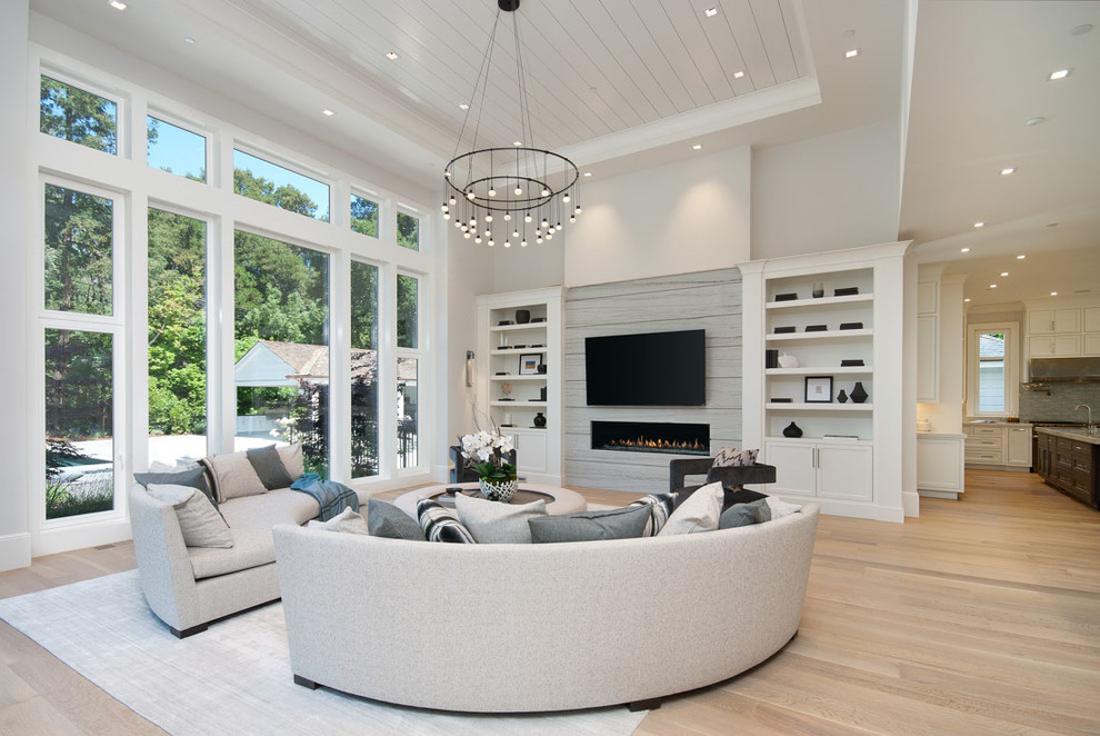 Imagen de sala de estar abierta tradicional renovada con paredes grises, suelo de madera clara, chimenea lineal, televisor colgado en la pared y suelo beige