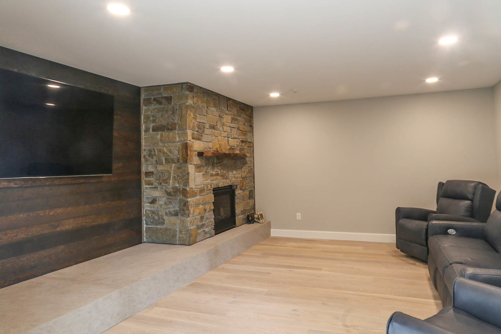 Cette photo montre une salle de séjour chic de taille moyenne et fermée avec un mur gris, parquet clair, une cheminée standard, un manteau de cheminée en pierre, un téléviseur fixé au mur et un sol beige.