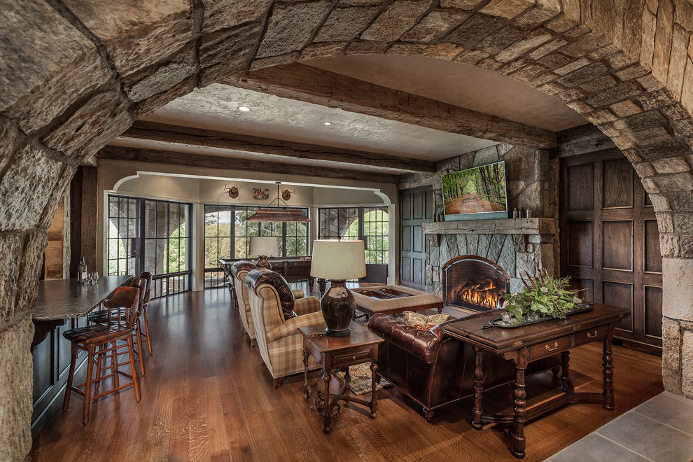 Photo of an expansive rustic open plan games room in Other with medium hardwood flooring, a standard fireplace, a stone fireplace surround, a game room, beige walls and a wall mounted tv.
