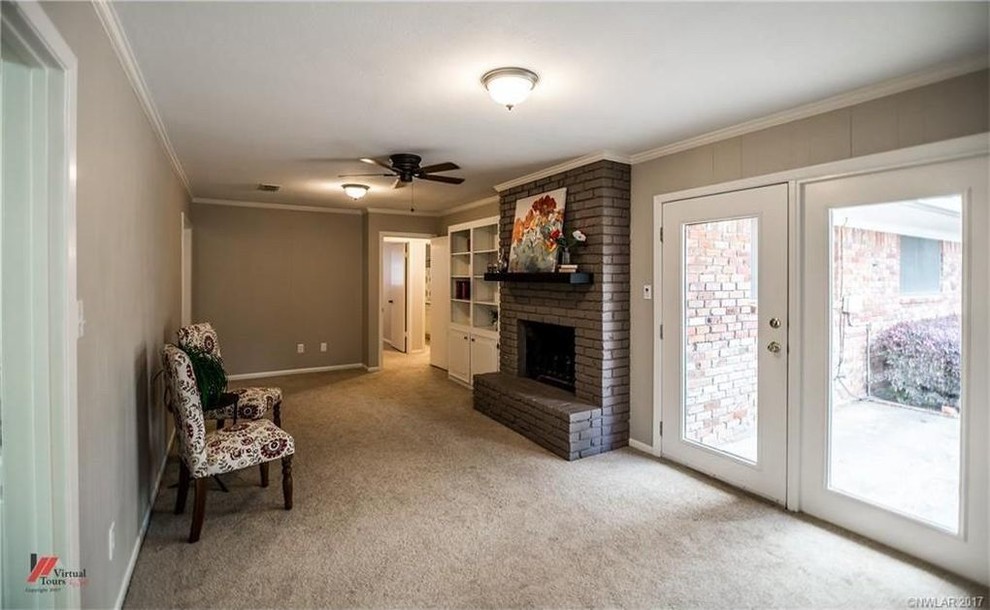 Cette photo montre une petite salle de séjour chic ouverte avec une bibliothèque ou un coin lecture, un mur beige, moquette, une cheminée standard, un manteau de cheminée en brique et un sol beige.