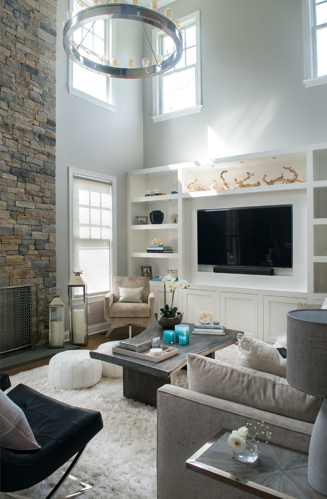 Aménagement d'une grande salle de séjour classique ouverte avec un mur gris, parquet foncé, une cheminée standard, un manteau de cheminée en pierre, un téléviseur encastré et un sol marron.