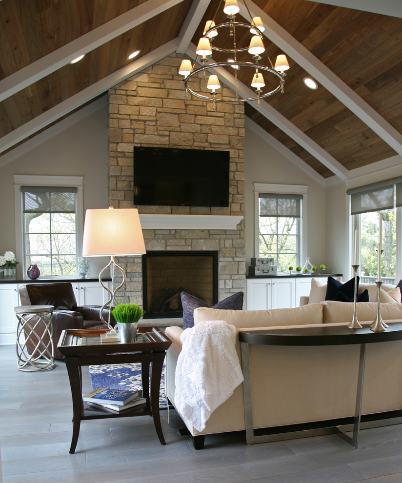 Example of a mid-sized classic open concept medium tone wood floor and gray floor family room design in Milwaukee with gray walls, a standard fireplace, a stone fireplace and a wall-mounted tv