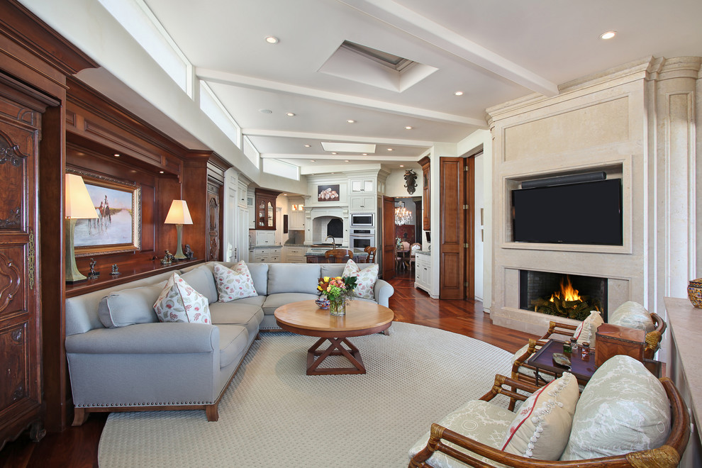 Diseño de sala de estar abierta clásica con paredes beige, suelo de madera oscura, todas las chimeneas y televisor colgado en la pared
