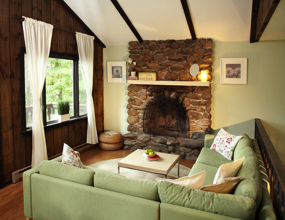 Example of a classic medium tone wood floor family room design in Other with green walls, a standard fireplace, a stone fireplace and no tv