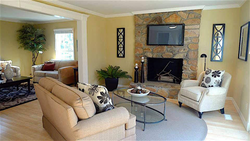 他の地域にある広いトランジショナルスタイルのおしゃれなオープンリビング (黄色い壁、淡色無垢フローリング、標準型暖炉、石材の暖炉まわり、壁掛け型テレビ、茶色い床) の写真