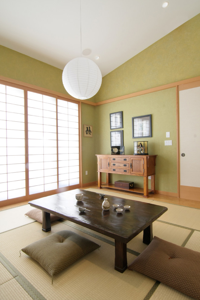 Diseño de sala de estar cerrada asiática grande sin chimenea con paredes verdes, televisor retractable y suelo de madera clara