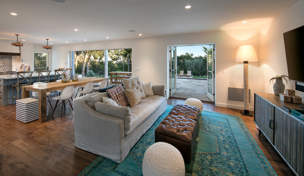 Modelo de sala de estar abierta mediterránea grande sin chimenea con paredes blancas, suelo de madera oscura, televisor colgado en la pared y suelo marrón