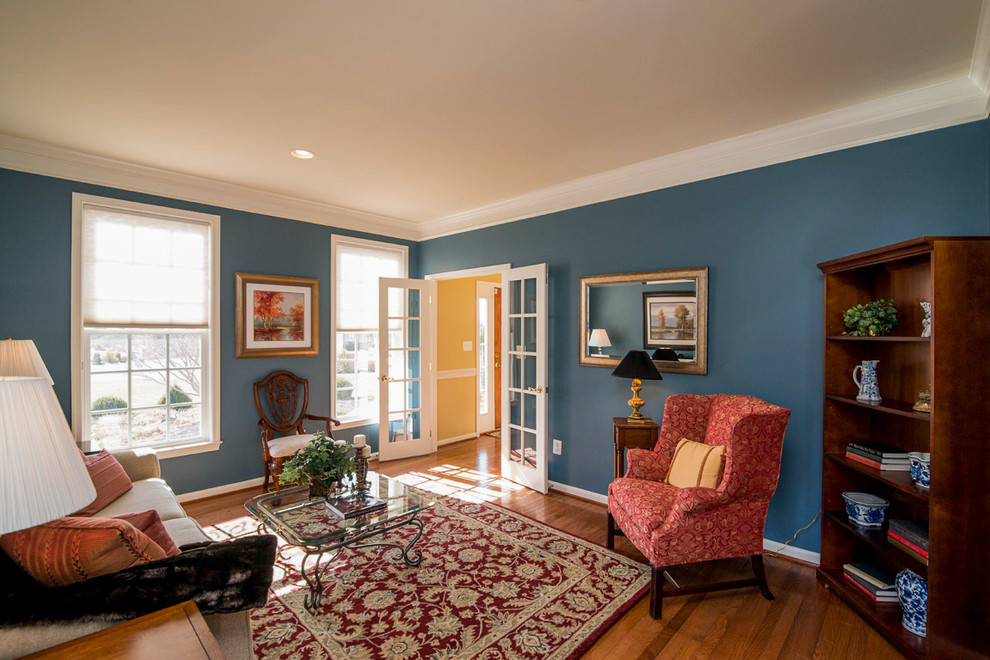 Cette photo montre une grande salle de séjour chic fermée avec un mur bleu, un sol en bois brun et aucune cheminée.