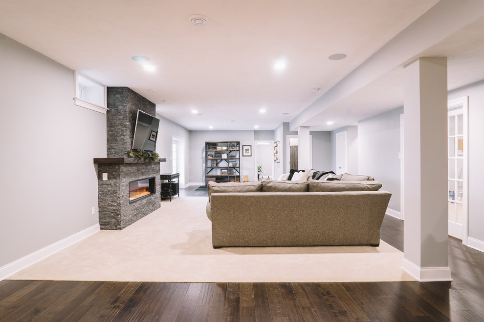 This is an example of a large classic open plan games room in Other with grey walls, dark hardwood flooring, a standard fireplace, a stone fireplace surround and a wall mounted tv.