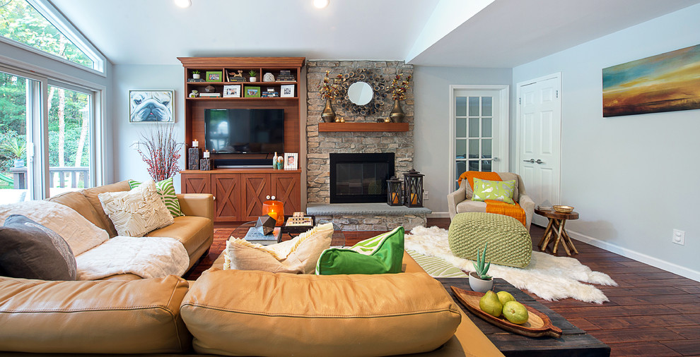 Cette image montre une grande salle de séjour traditionnelle ouverte avec un sol en bois brun, une cheminée standard, un manteau de cheminée en pierre, un téléviseur encastré, un mur gris, un sol marron et un plafond voûté.