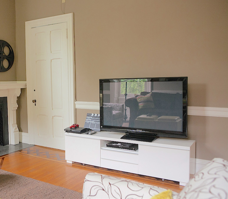 Foto de sala de estar tradicional renovada de tamaño medio con suelo de madera clara, chimenea de esquina, marco de chimenea de piedra y televisor independiente