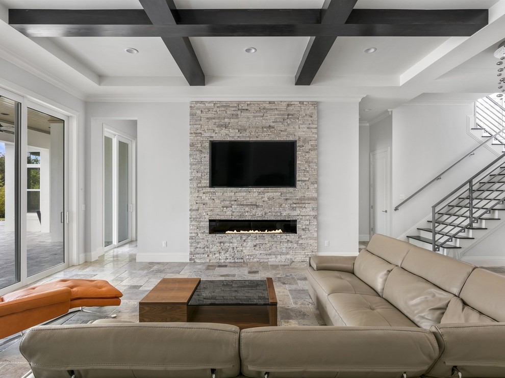 Diseño de sala de estar abierta minimalista grande con suelo de travertino, chimenea lineal, marco de chimenea de piedra, televisor colgado en la pared, suelo gris y paredes grises