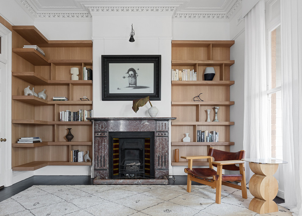 Пример оригинального дизайна: большая изолированная гостиная комната в стиле неоклассика (современная классика) с с книжными шкафами и полками, белыми стенами, стандартным камином, фасадом камина из камня, черным полом и деревянным полом без телевизора