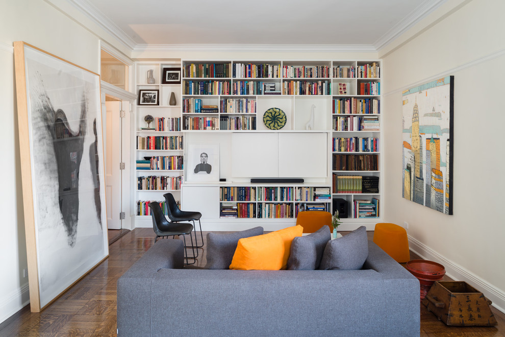 Modelo de sala de estar con biblioteca cerrada tradicional renovada con paredes beige, suelo de madera en tonos medios y televisor retractable