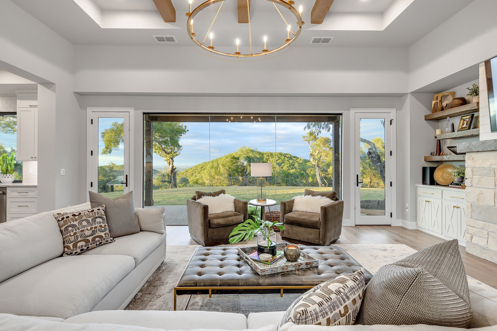 Example of a transitional light wood floor and tray ceiling family room design in Austin with gray walls, a stone fireplace and a wall-mounted tv