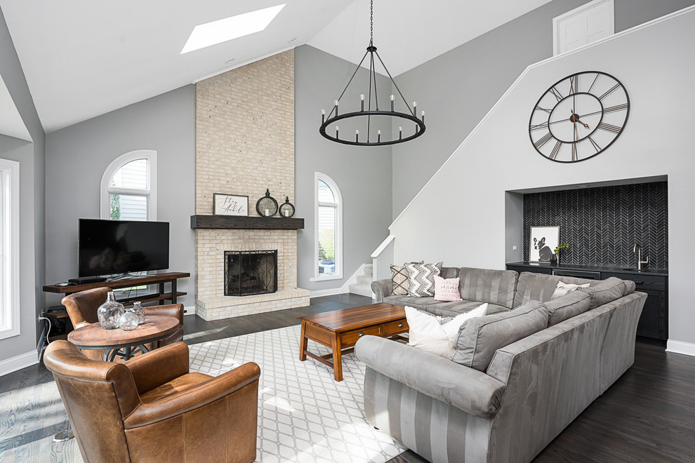 Immagine di un ampio soggiorno chic aperto con pareti grigie, parquet chiaro, cornice del camino in mattoni, TV autoportante e pavimento grigio