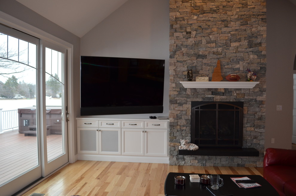 Imagen de sala de estar abierta clásica renovada grande con paredes grises, suelo de madera clara, todas las chimeneas, marco de chimenea de piedra, televisor colgado en la pared y suelo marrón