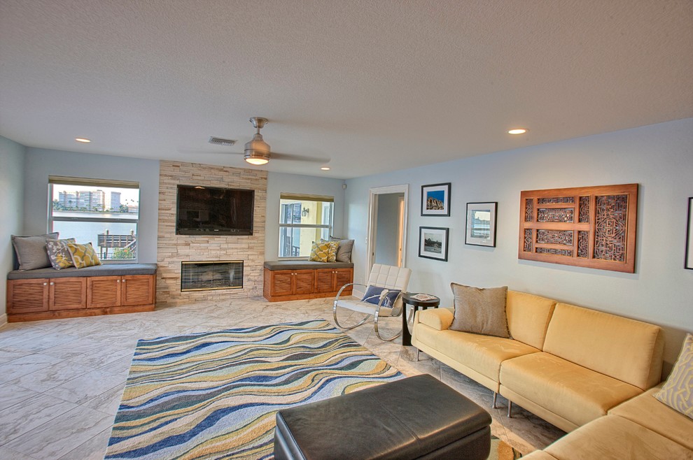 Modelo de sala de estar tradicional renovada grande con paredes azules, todas las chimeneas, marco de chimenea de piedra, televisor colgado en la pared y suelo de baldosas de porcelana