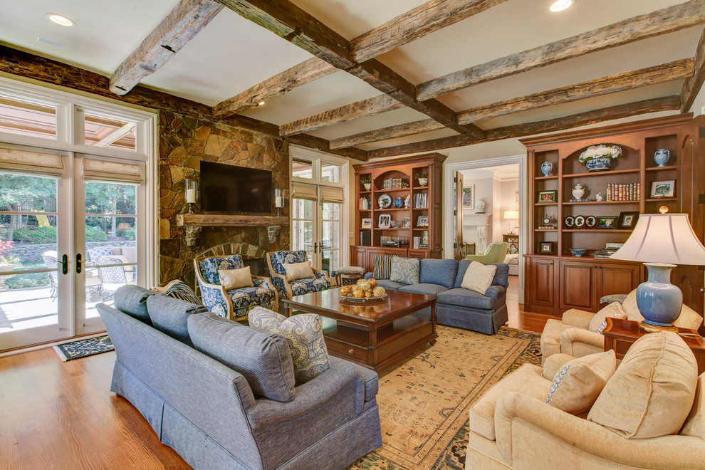 Imagen de sala de estar abierta clásica grande con paredes beige, suelo de madera clara, todas las chimeneas, marco de chimenea de piedra y televisor colgado en la pared
