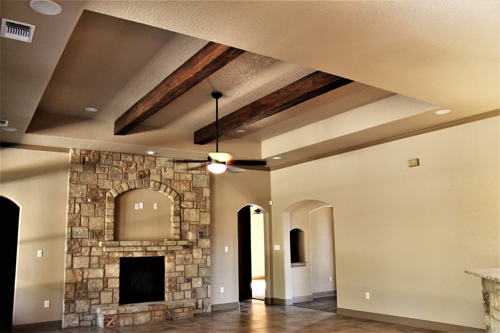 Пример оригинального дизайна: большая открытая гостиная комната в классическом стиле с бежевыми стенами, полом из керамогранита, стандартным камином, фасадом камина из камня, телевизором на стене и коричневым полом