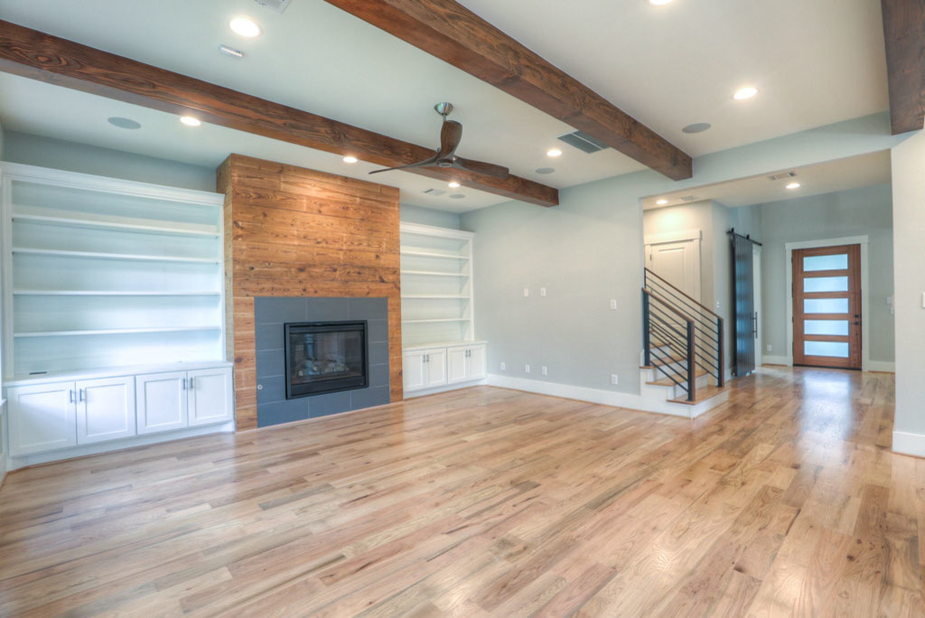Großes, Offenes Retro Wohnzimmer mit grauer Wandfarbe, braunem Holzboden, Kamin, Kaminumrandung aus Stein, TV-Wand und braunem Boden in Houston
