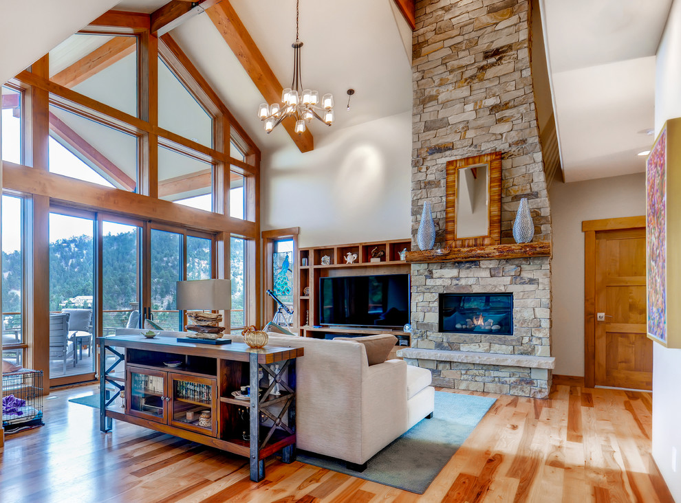 Exemple d'une grande salle de séjour montagne ouverte avec un sol en bois brun, une cheminée standard, un manteau de cheminée en pierre et un mur beige.