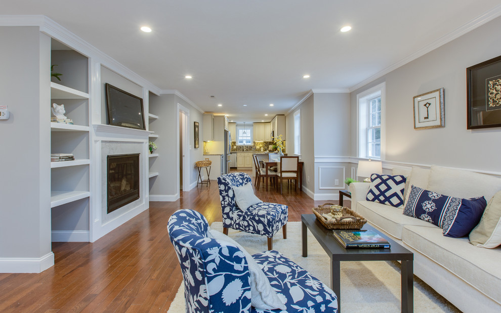 Mittelgroßes, Offenes Klassisches Wohnzimmer mit grauer Wandfarbe, braunem Holzboden, Kamin, Kaminumrandung aus Stein, TV-Wand und braunem Boden in Boston