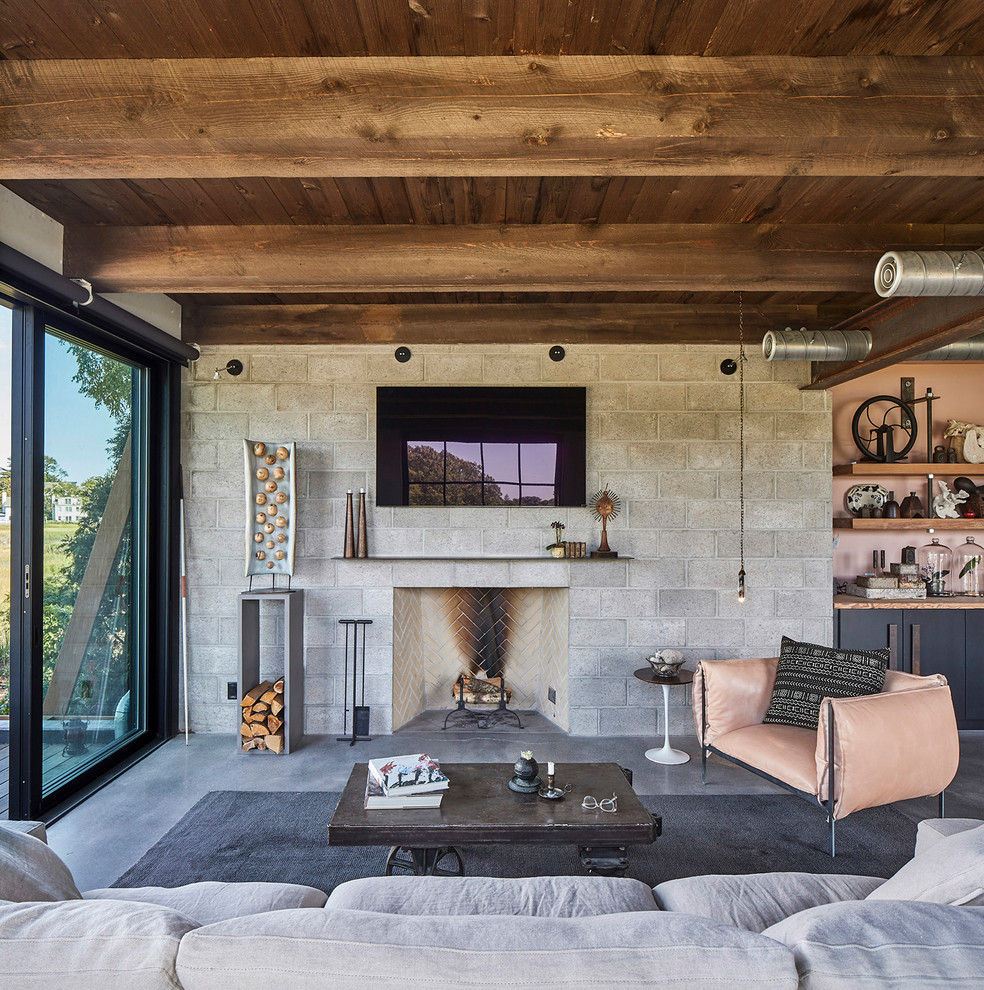Идея дизайна: открытая гостиная комната в стиле лофт с серыми стенами, бетонным полом, стандартным камином, фасадом камина из камня, телевизором на стене, серым полом и ковром на полу