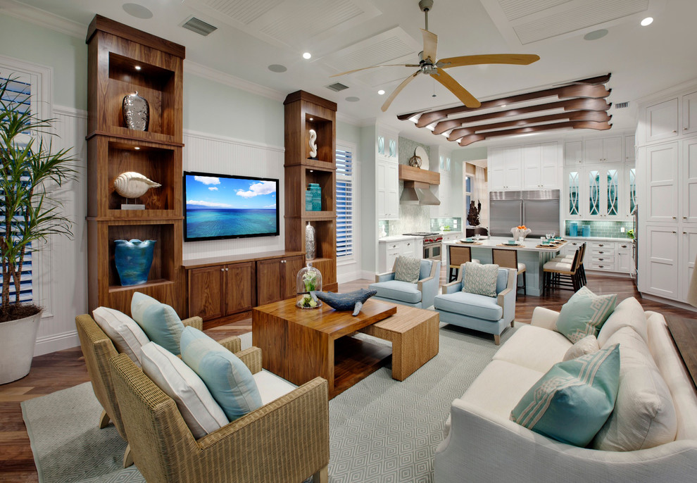 Modelo de sala de estar abierta tropical grande con paredes azules, suelo de madera en tonos medios y televisor colgado en la pared