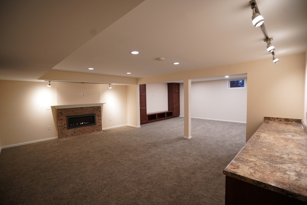 На фото: открытая гостиная комната среднего размера в классическом стиле с бежевыми стенами, ковровым покрытием, горизонтальным камином, фасадом камина из кирпича, телевизором на стене и разноцветным полом