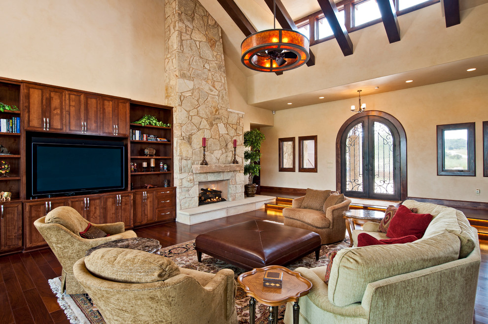 Inspiration for an expansive mediterranean open plan games room in Austin with beige walls, medium hardwood flooring, a standard fireplace, a stone fireplace surround and a concealed tv.