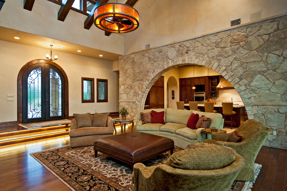 Стильный дизайн: огромная открытая гостиная комната в средиземноморском стиле с бежевыми стенами, паркетным полом среднего тона, стандартным камином, фасадом камина из камня и скрытым телевизором - последний тренд